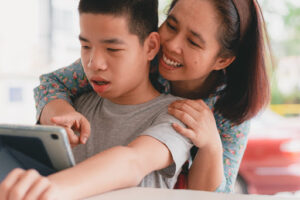 A mom smiling with her special needs son, a person for whom she established a supplemental needs trust, and showing something on a tablet.