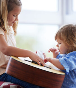 Two children playing with a guitar, content because of probate guardianship that has ensured they are safe, healthy, and happy.