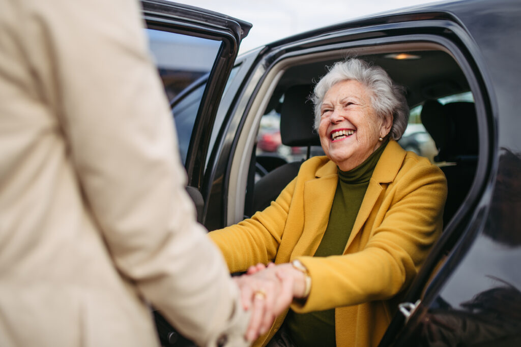 A senior woman being helped out of her car, happy and enjoying retirement stress-free after their child answered the question, How do I monitor my elderly parents’ finances?