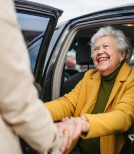 A senior woman being helped out of her car, happy and enjoying retirement stress-free after their child answered the question, How do I monitor my elderly parents’ finances?